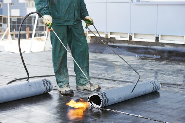 Roofer installing Roofing felt with heating and melting of bitumen roll by torch on flame during roof repair